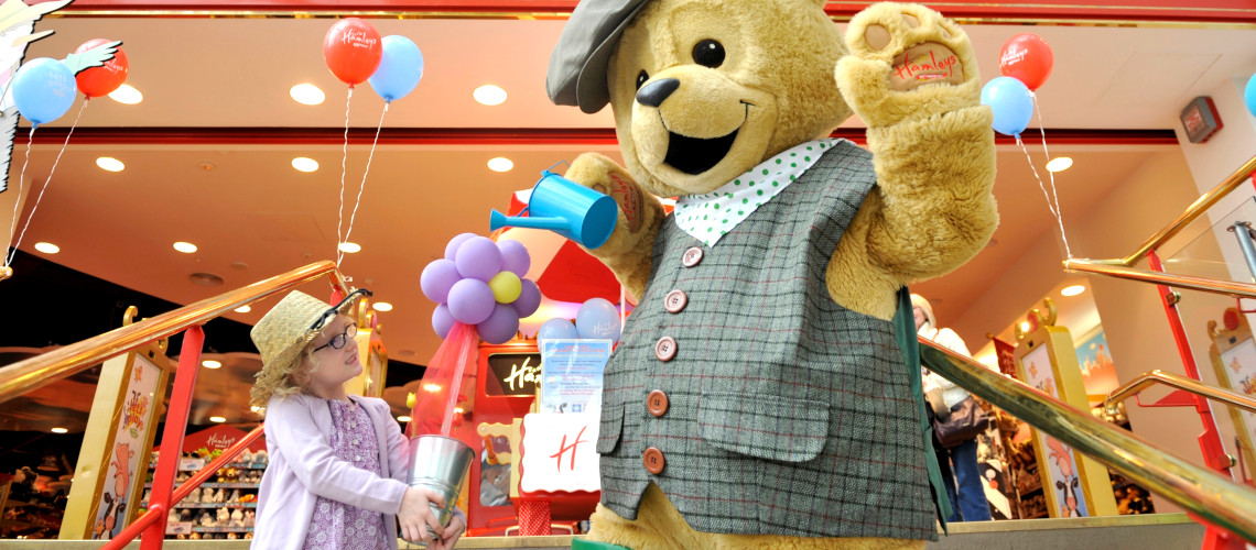 A babygirl plays with a giant teddy bear in front of the Hamleys store in London