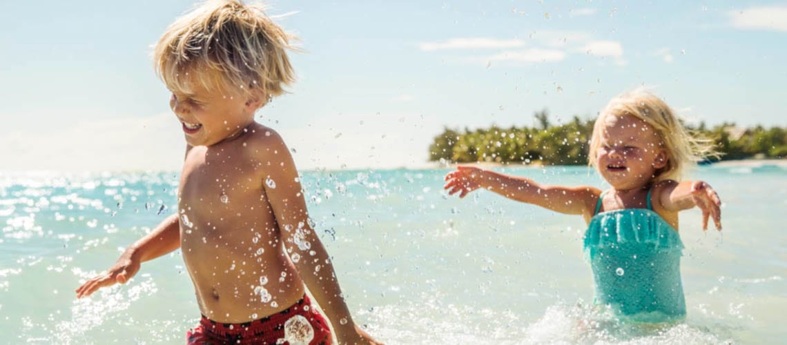 Un enfant et sa petite soeur jouent ensemble dans l'eau translucide d'une île paradisiaque